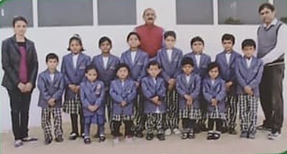 A class of children in navy blazers standing with their teachers.