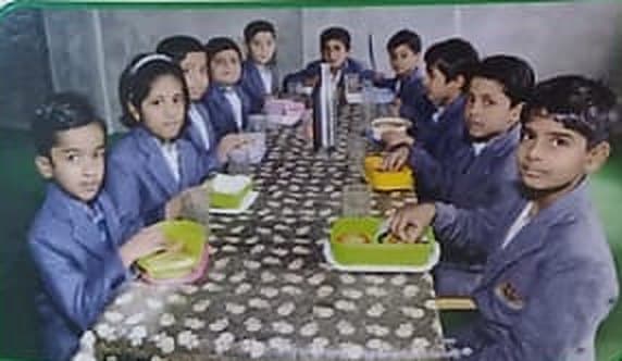 Students in blazers sharing lunch at a long table.