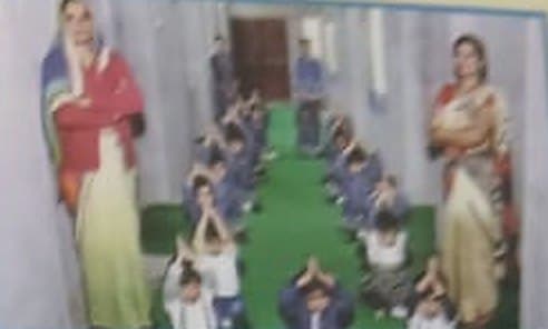 Children with folded hands in rows during a morning prayer, teachers standing at either side.