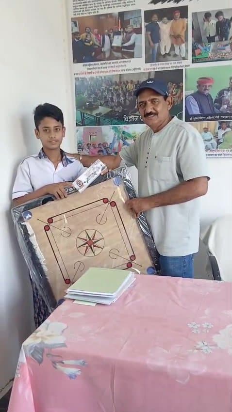 A student receiving a prize from a guest in front of a wall of school photographs.